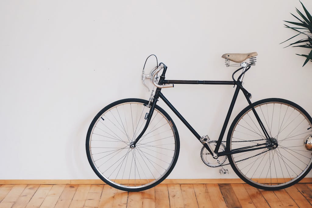 A vintage-style bicycle leaning against a clean white wall with wooden flooring, emphasizing minimalist design.
