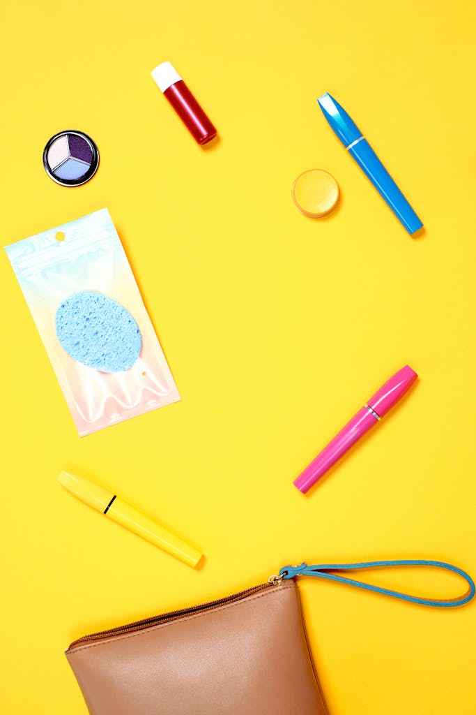 Colorful flatlay of makeup products and accessories on a bright yellow background.